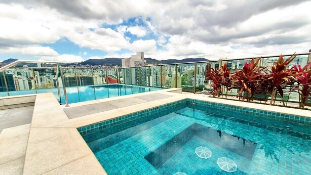 Una piscina en la azotea con baldosas azules cristalinas, rodeada por una barandilla de cristal y plantas rojas.