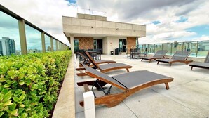 Una terraza con sillones de sol, un edificio de diseño moderno y vistas al horizonte de la ciudad.