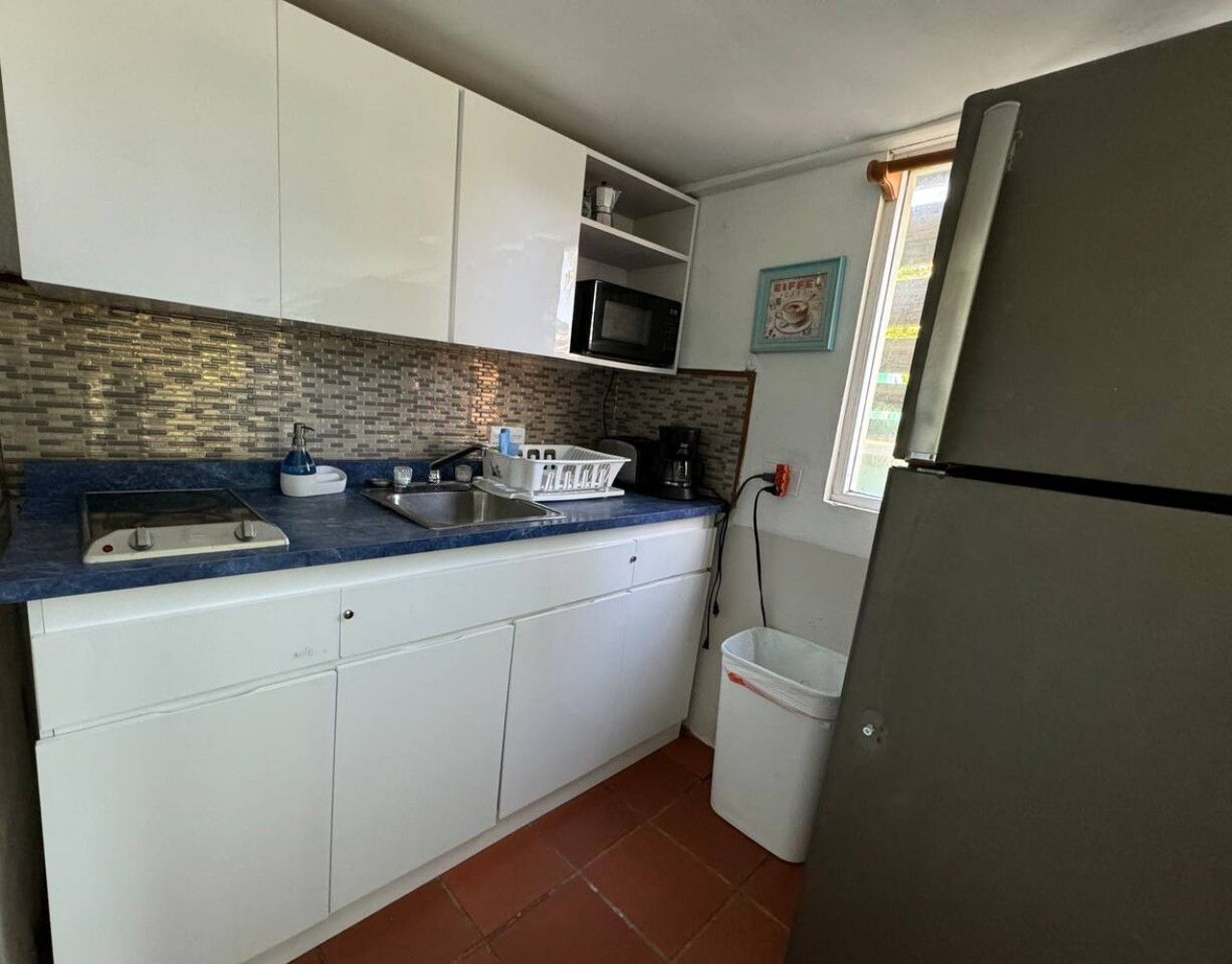 A compact kitchen with white cabinets, a blue countertop, a microwave, a sink, and a refrigerator.