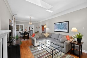 Ein modernes Wohnzimmer mit einem Ecksofa, einem Glastisch und einem Essbereich mit einer Chandelier.