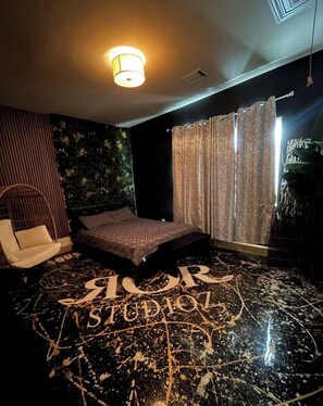 A bedroom with a bed, a chair, a wall-mounted plant, and a ceiling light. - Spacious and Lux 2 BR With Game Room & Hot Tub + Gated Community (Houston)