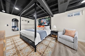 Ein modernes Schlafzimmer mit einem Himmelbett, einem gestreiften Sessel, einem Nachttisch und einem an der Wand befestigten Fernseher.