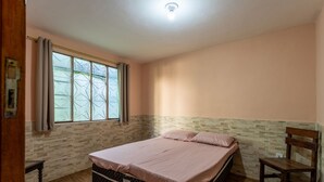 A bedroom with a bed, a window with curtains, a wooden chair, and a tiled floor. - Casa com Churrasqueira a 550m da Praia do Saco (Mangaratiba)