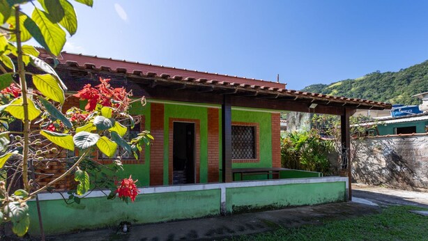 A house with a green and red exterior, a covered porch, and a garden with red flowers. - Casa com Churrasqueira a 550m da Praia do Saco (Mangaratiba)