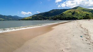 A beach with a clear sky, calm water, and a hilly landscape in the background. - Casa com Churrasqueira a 550m da Praia do Saco (Mangaratiba)