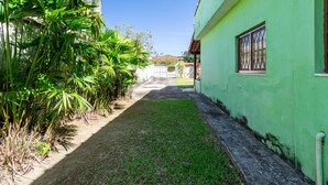 A narrow pathway leading to a green building with a window, surrounded by lush greenery. - Casa com Churrasqueira a 550m da Praia do Saco (Mangaratiba)