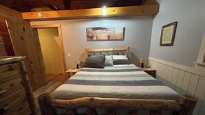 A wooden-framed bed with a striped bedspread, a nightstand with a lamp, and a painting on the wall. - Merry Grinchmas! Theme getaway, limited availability!! Free photo ops! (Embden)