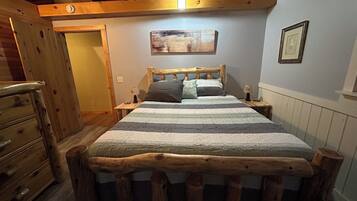 A wooden-framed bed with a striped bedspread, a nightstand with a lamp, and a painting on the wall.
