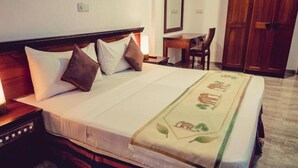 Una cama bien hecha con una colcha decorativa, una mesita de noche con lámpara, un escritorio de madera y un armario en una habitación de hotel.