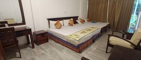 A hotel room with a large bed, a desk, a chair, and a window with curtains.
