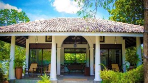 Un espacio de descanso al aire libre cubierto, con techo de baldosas, columnas y un banco.