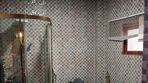 A bathroom with a checkered tile wall, a glass shower enclosure, a toilet, and a bathtub. - Zion Apartment  (Old-Yundum)
