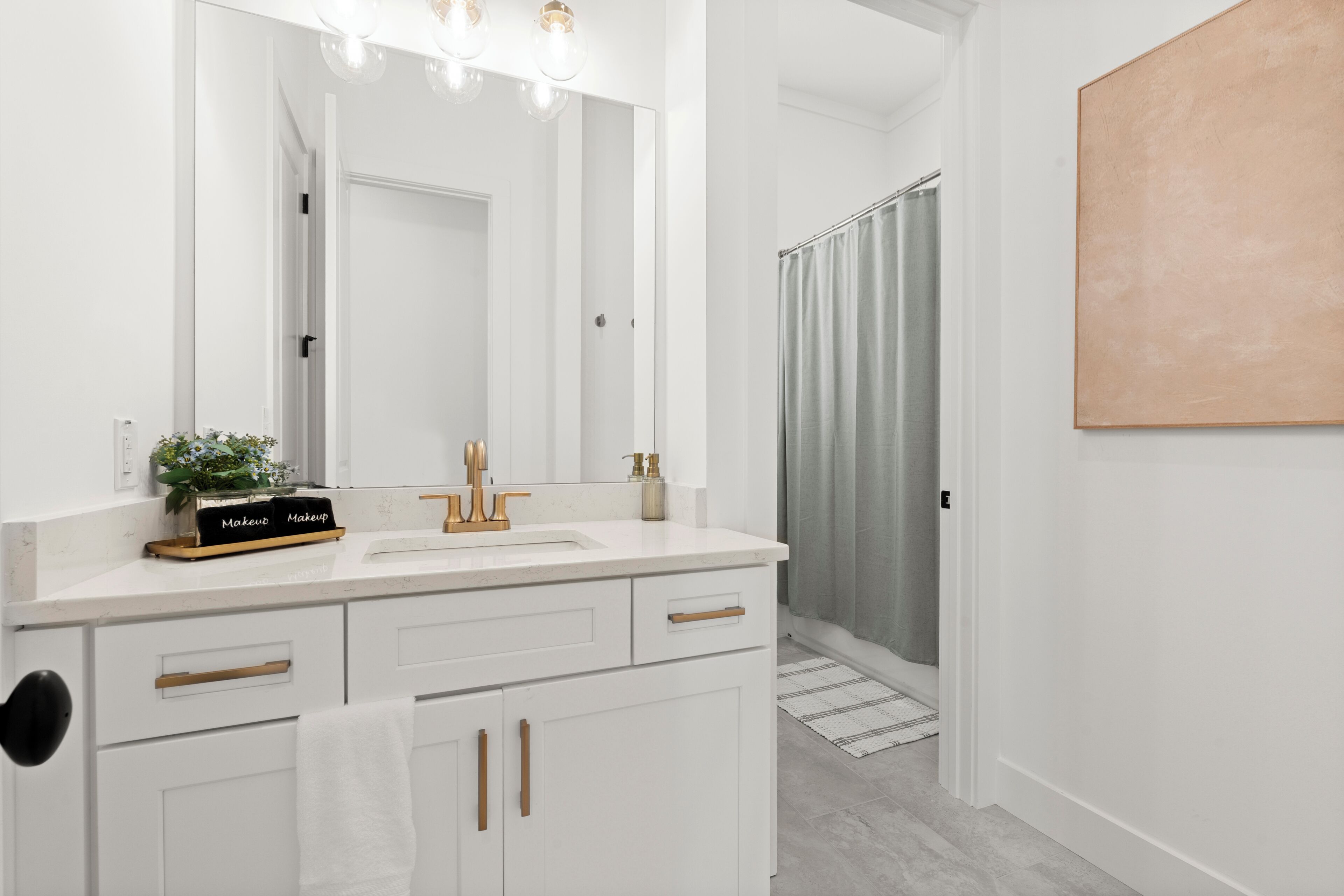 Un baño con tocador blanco, espejo, lavabo y cortina de ducha.