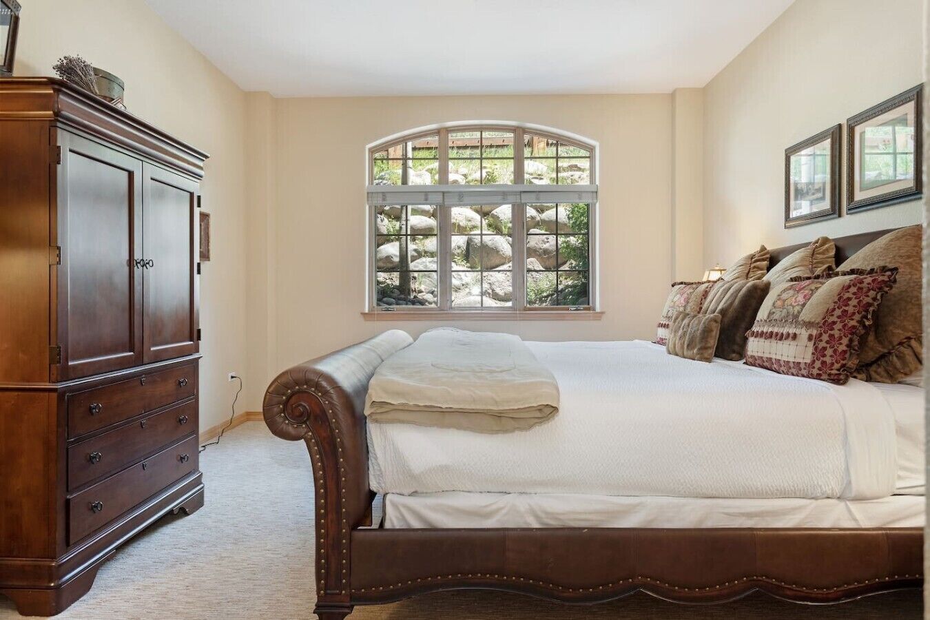 A bedroom with a large bed, a dresser, a window with a view of rocks, and two framed pictures on the wall.