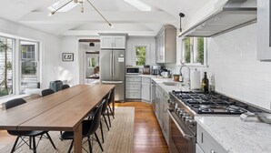 A modern kitchen with a dining area, stainless steel appliances, and a large window. - The School Street House • Dock Square Village (Kennebunkport)
