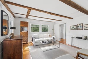 Un salon spacieux avec un canapé blanc, des poutres en bois, de grandes fenêtres et une table basse moderne.