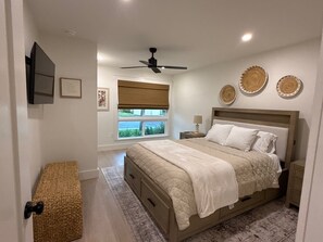 A bedroom with a bed, bedside tables, a ceiling fan, a window with blinds, and decorative wall plates. - Runaway Bay 192 - Direct bayfront, beach, pool and gym (Bradenton Beach)
