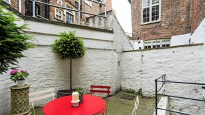A red table with a candle, white chairs, a potted plant, and a white wall in a courtyard. - No 2 Precentors Court (York)
