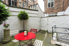 Ein roter Tisch mit Kerze, weiße Stühle, ein Topfpflanze und eine weiße Wand in einem Innenhof.