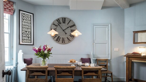A dining area with a wooden table, chairs, a large wall clock, and a framed inspirational quote. - No 2 Precentors Court (York)
