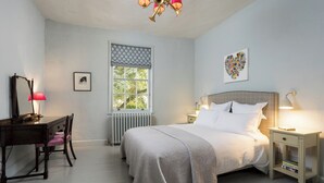 A bedroom with a bed, bedside tables, a desk, a chair, a radiator, a window with a patterned curtain, and a wall art piece. - No 2 Precentors Court (York)