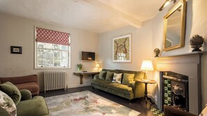 A living room with a green sofa, a fireplace, a radiator, and a large window with a red valance. - No 2 Precentors Court (York)