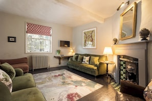 Ein Wohnzimmer mit einem grünen Sofa, einem Kamin, einem Heizkörper und einem großen Fenster mit rotem Vorhang.