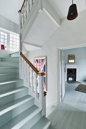 Eine Treppe mit weißen Balustraden, einer schwarzen Pendelleuchte, einem Union Jack im Bilderrahmen und einem Kamin mit Teppich.