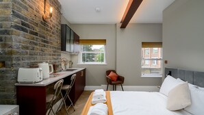 Een hotelkamer met een bakstenen muur, een bed, een bureau met een stoel, een raam en uitzicht op een gebouw.