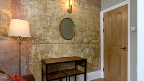 Een kamer met een muur met een vintage uitstraling, een ronde spiegel, een houten deur, een vloerlamp en een klein houten tafeltje.