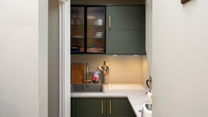 A kitchen with a sink, green cabinets, and a window with blinds. - Brixton Lofts - Deluxe Studio (No.2) (London)