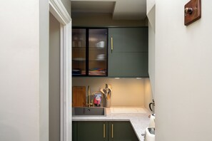 A kitchen with a sink, green cabinets, and a window with blinds. - Brixton Lofts - Deluxe Studio (No.2) (London)