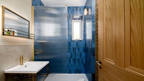 Une salle de bain avec un lavabo blanc, une cabine de douche en verre et une porte en bois.