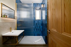 Ein Badezimmer mit einem weißen Waschbecken, einer Duschkabine aus Glas und einer Holztür.