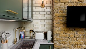 Une cuisine équipée d’un évier, de meubles de rangement verts, d’un grille-pain et d’un téléviseur fixé au mur.