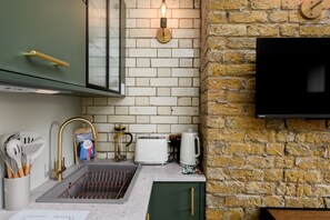 Eine Küche mit Spüle, grünen Schränken, einem Toaster und einem an der Wand montierten Fernseher.