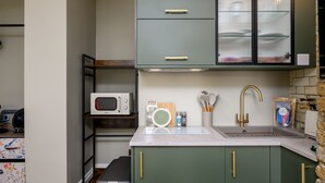 Une cuisine équipée d’un four à micro-ondes, d’un évier, de meubles de rangement verts et d’un plan de travail.
