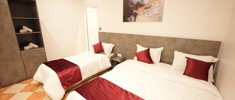 A hotel room with two beds, a wardrobe, a painting, and a check-in counter.