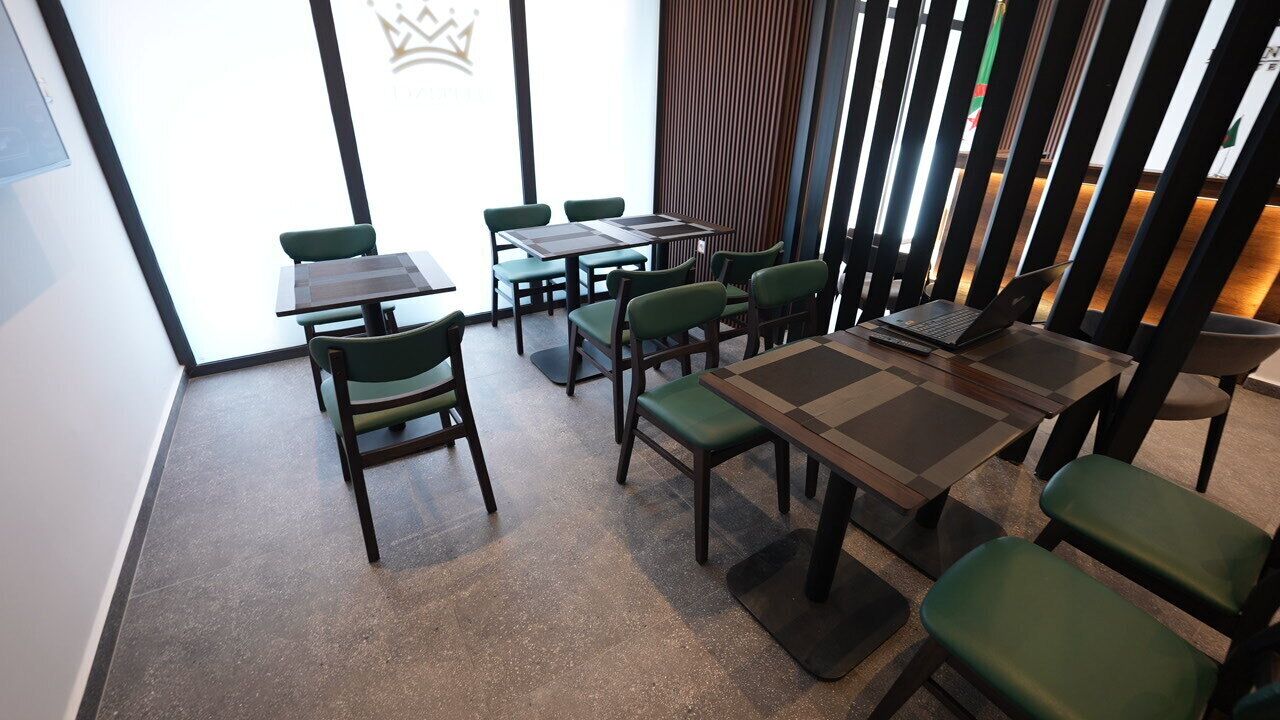 A modern interior with tables and chairs, a wooden partition, and a crown logo on the wall.