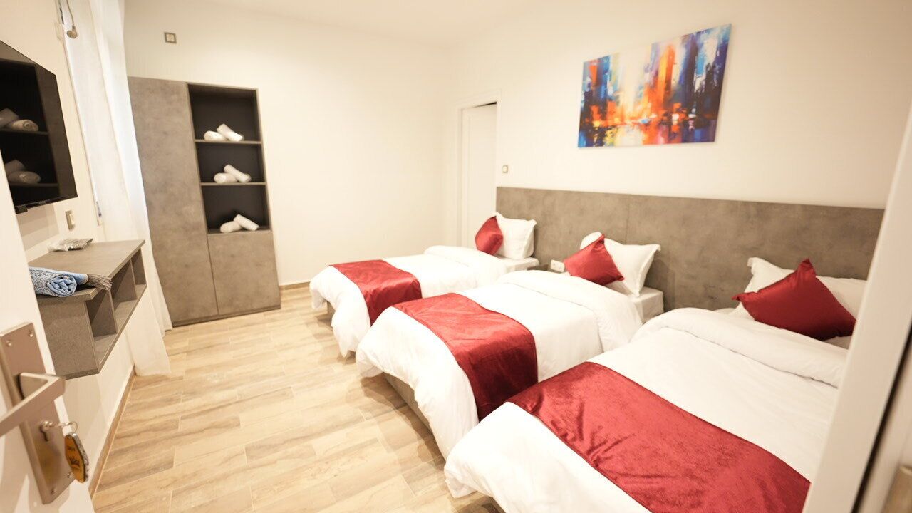 A hotel room with three beds, a TV, a wardrobe, and a painting on the wall.