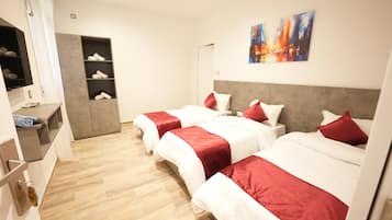 A hotel room with three beds, a TV, a wardrobe, and a painting on the wall.