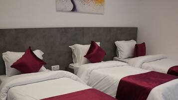 A hotel room with four beds, each with white bedding and red accents, a grey headboard, and a checkered floor.