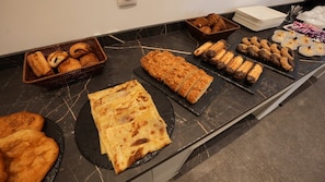 A buffet with various baked goods including pastries, bread, and desserts.