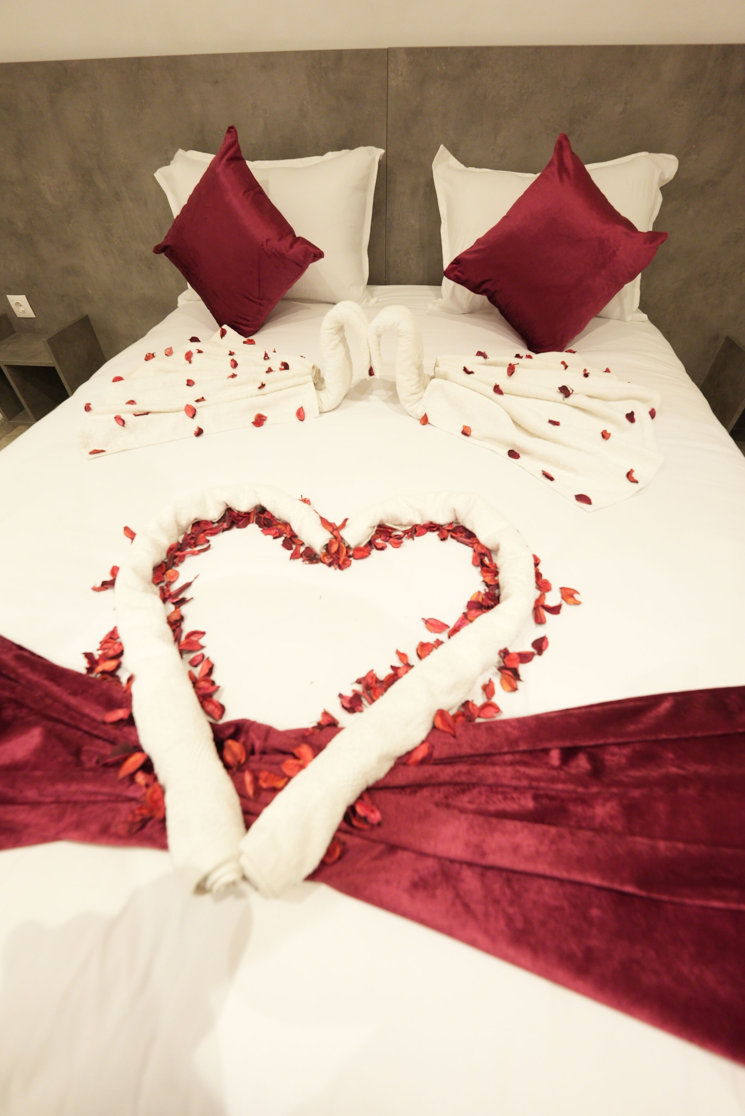 A bed with a heart-shaped arrangement of rose petals and a white towel.