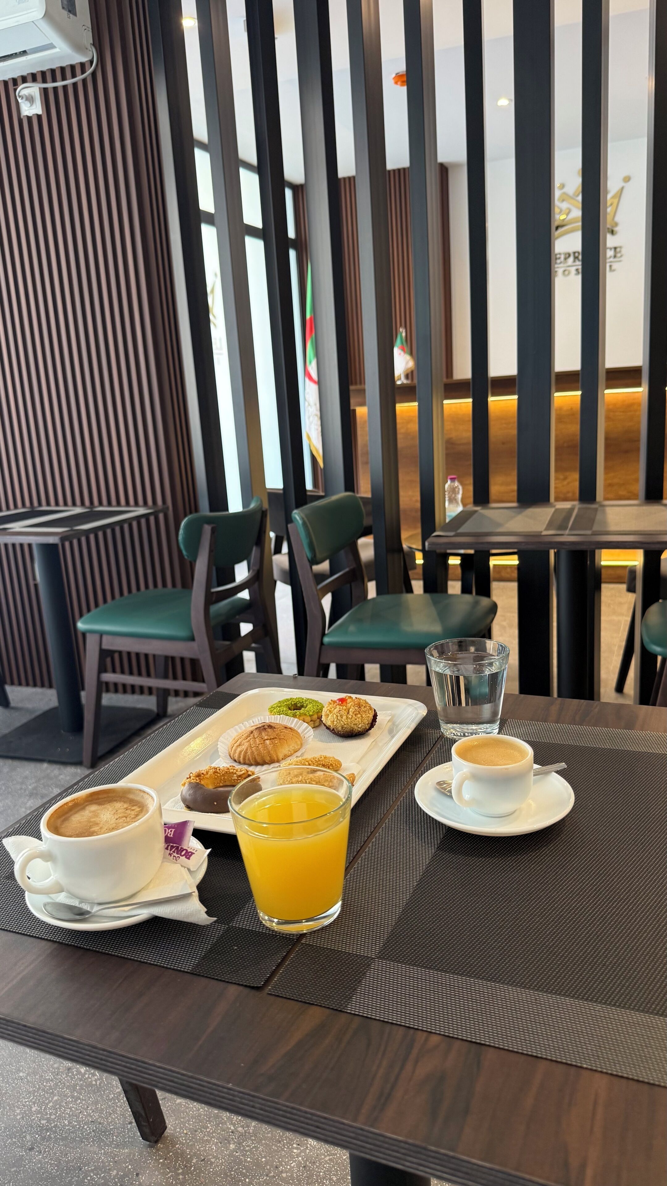 Un desayuno servido con una bandeja de pasteles, un vaso de jugo de naranja y dos tazas de café en una mesa.
