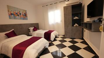Habitación de hotel con dos camas, suelo a cuadros, un cuadro en la pared y un televisor montado en la pared.