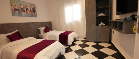 A hotel room with two beds, a checkered floor, a painting on the wall, and a TV mounted on the wall.