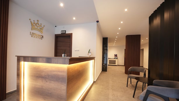Un mostrador de recepción de hotel con un logotipo de corona, un cartel que dice 'Director' encima y una zona de recepción con sillas y una mesita.
