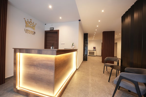A hotel reception desk with a crown logo, a 'Director' sign above it, and a reception area with chairs and a small table.
