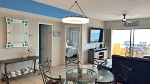 Ein Hotelzimmer mit Essbereich, einem Bett, einem Fernseher und einem Balkon mit Meerblick.